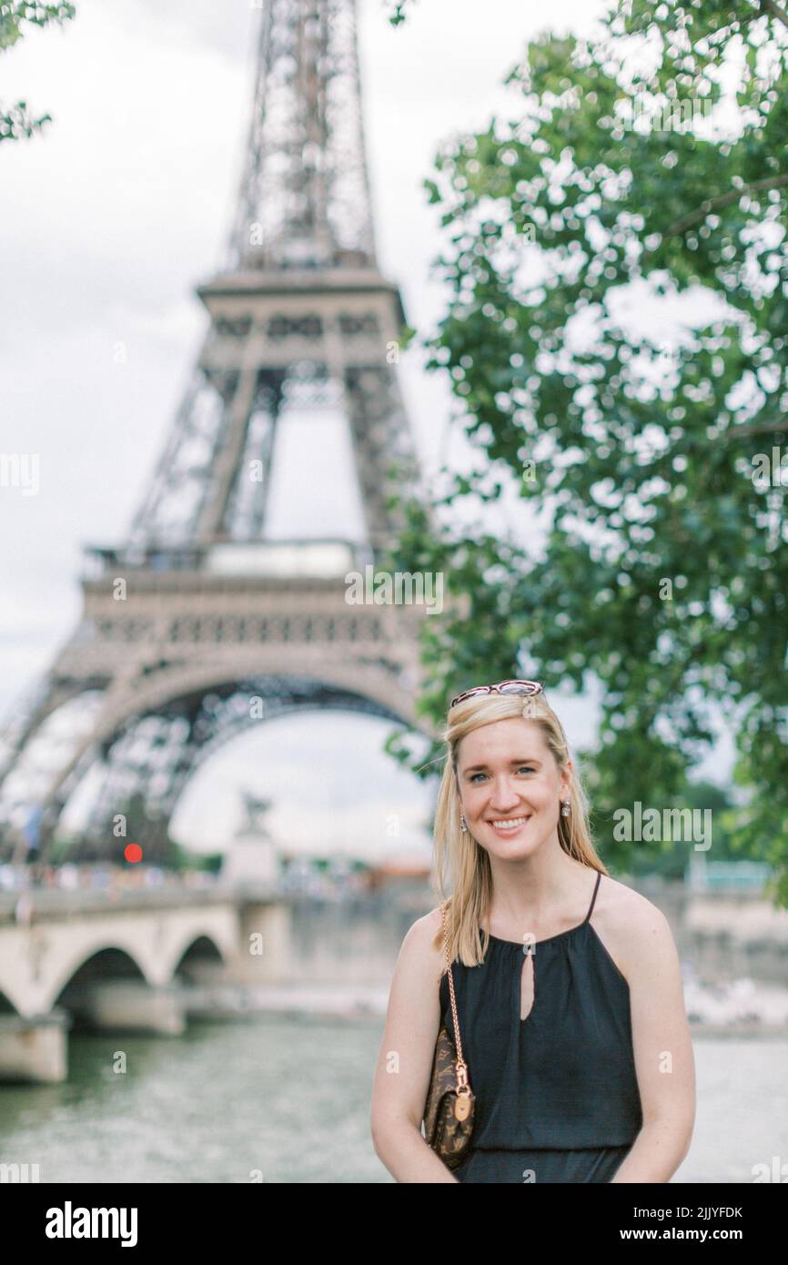 Blonde 30-something woman smiles in front of the Eiffel Tower in Paris Stock Photo