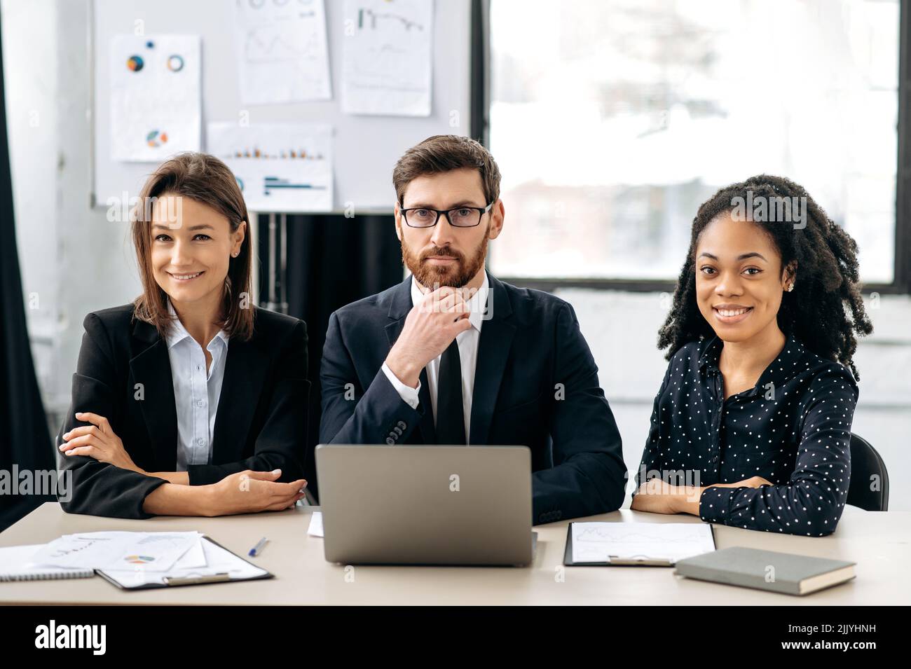 Successful business people. Multiracial influential business people in formal wear look at the camera, smiling. Elegant creative colleagues sitting in modern office, working together on project Stock Photo