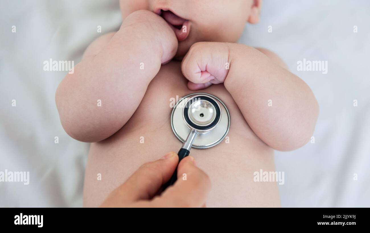 Female doctor examining baby boy toddler listening to lungs with stethoscope. A nurse having medical checkup with sick little newborn patient in clini Stock Photo
