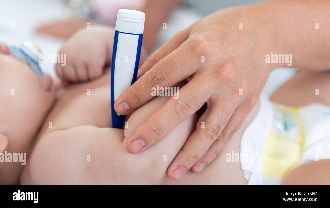 Doctor checking the temperature fever to small newborn with thermometer. Cute boy and chubby hands of a child. A newborn age of 3 months. Pediatrician Stock Photo