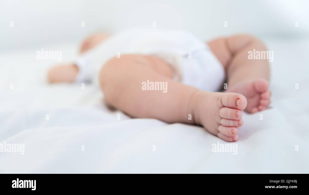 Newborn chubby foots over white background. Close up new born baby body part. Peace calm infant toddler boy laying on soft white blanket. Family mater Stock Photo