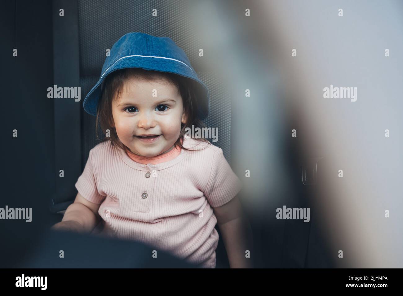 Baby girl wearing hat sitting in car looking at camera, enjoying the journey to the mountains. Stock Photo