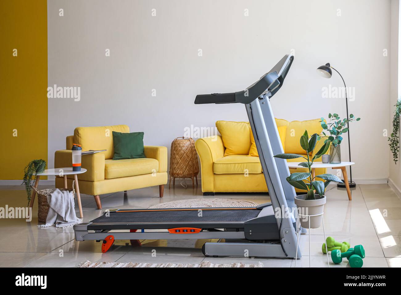 Interior of light living room with treadmill, sofa and armchair Stock