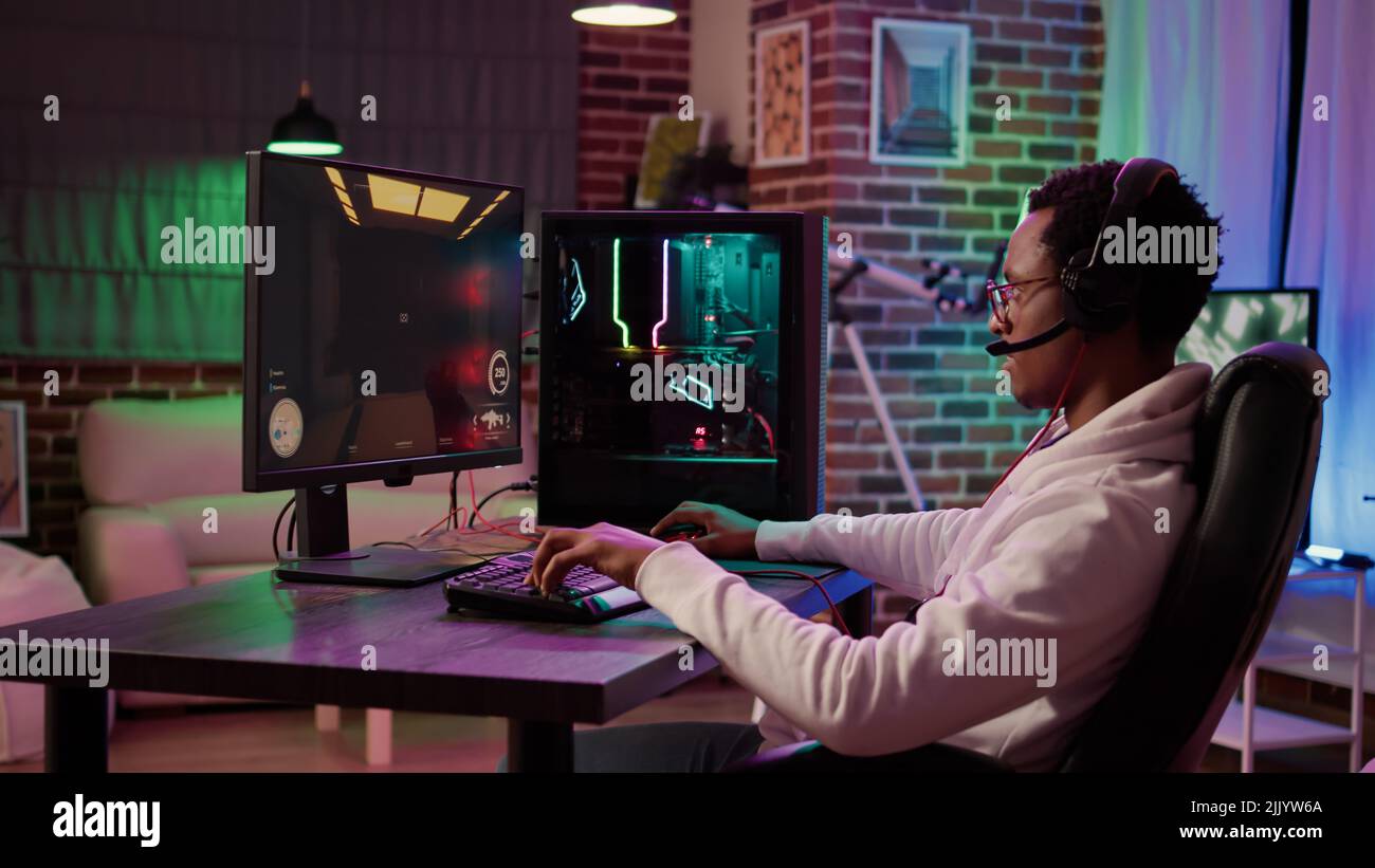 African american man pc gaming setup relaxing playing multiplayer online action game talking to team on headset in tournament. Gamer streaming first person shooter while explaining gameplay Stock Photo - Alamy