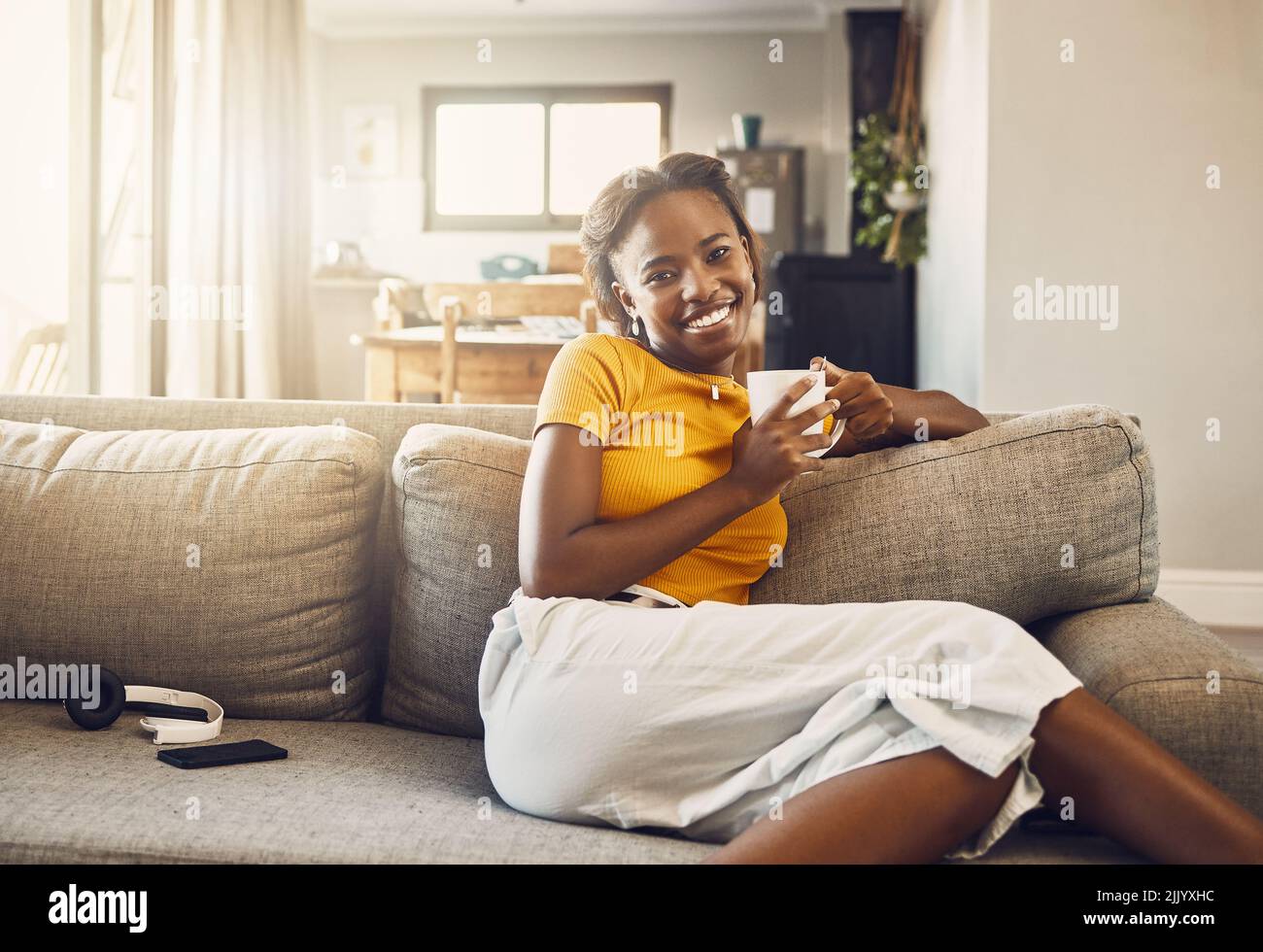 Beautiful, pretty and happy woman relaxing, drinking coffee and resting on the couch in the living room alone at home. Portrait of a smiling, cheerful Stock Photo