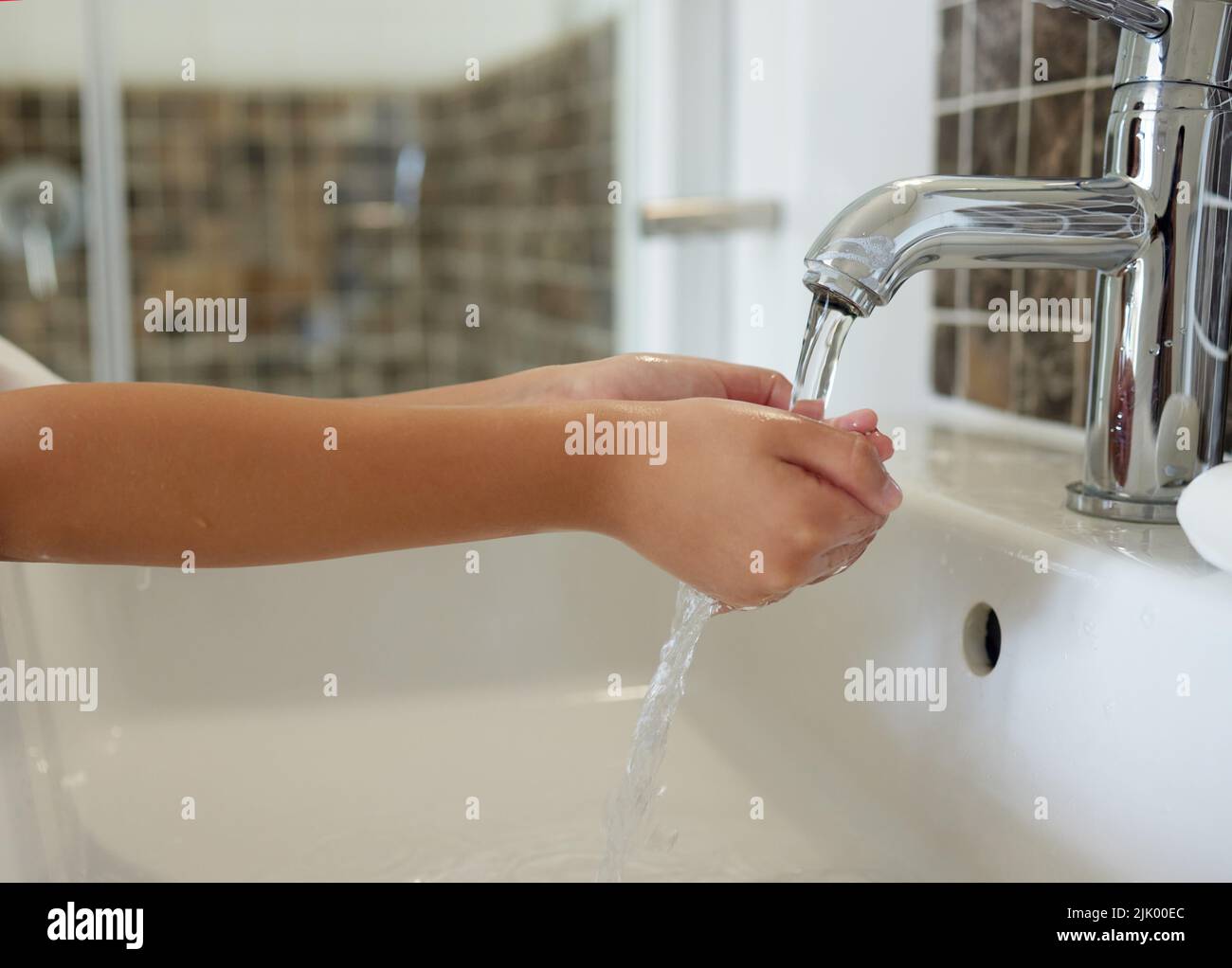 A closeup of a child washing her hands at the sink inside a bathroom with running tap water. A kid practicing hygiene and cleanliness by cleaning her Stock Photo