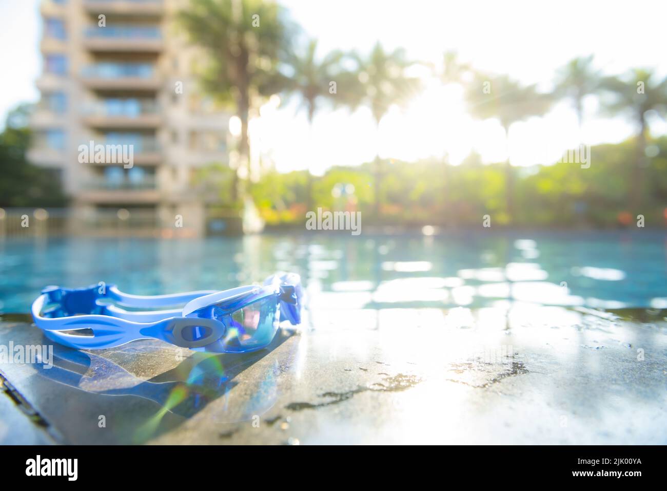 swimming goggles on the side of a swimming pool in a morning with a rising sun at horizontal composition Stock Photo