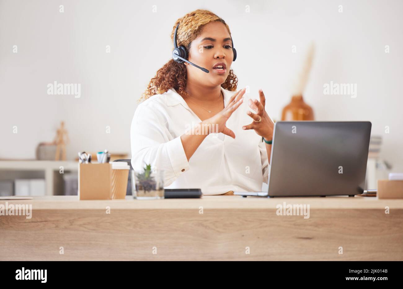 Female call center agent talking on headset while doing a video or zoom call and working in an office. Businesswoman consulting and explaining while Stock Photo