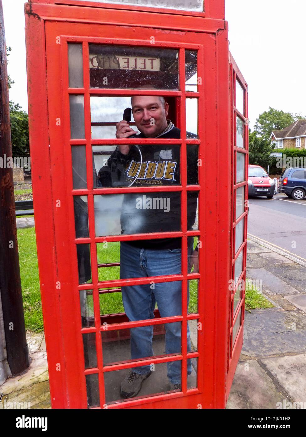 A man making a call in an iconic red telephone booth in Harmondsworth, Hillingdon, Middlesex, London, England, UK. Stock Photo