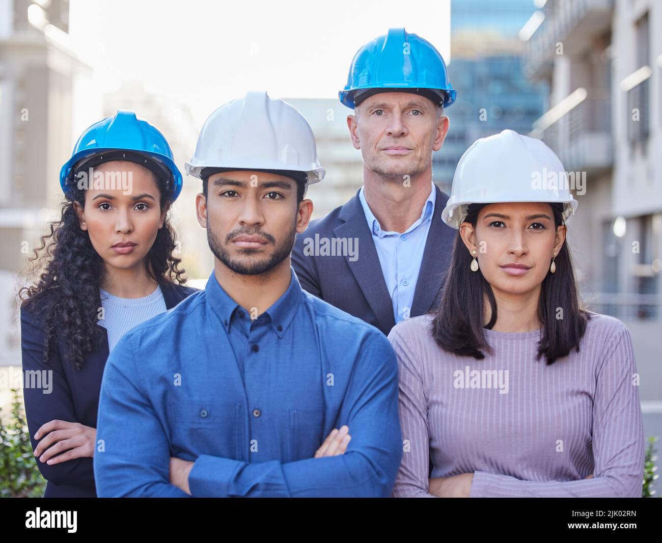There isnt a challenge we cant overcome. a diverse group of businesspeople standing together with their arms folded while wearing hardhats. Stock Photo
