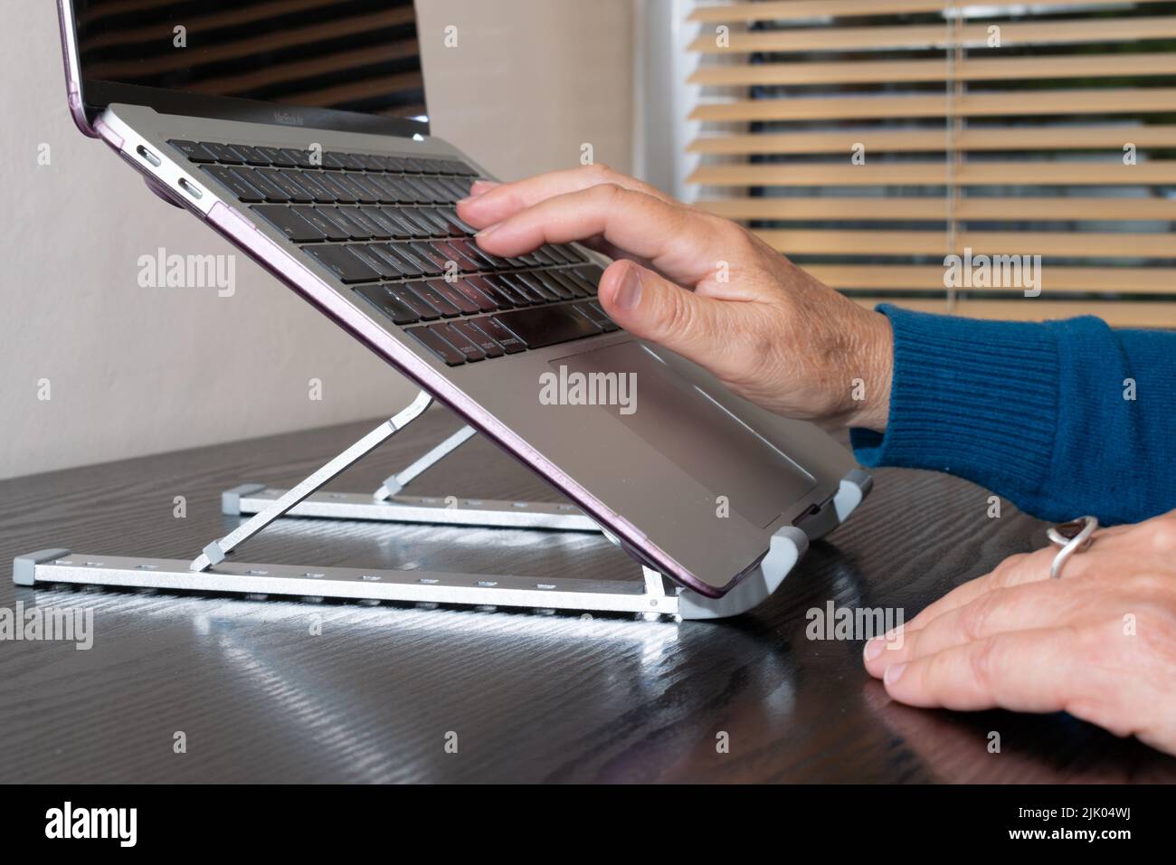 Laptop stand for wrist protection and neck posture. Foldable adjustable stand with hand typing on laptop screen raised to eye height in home office. Stock Photo
