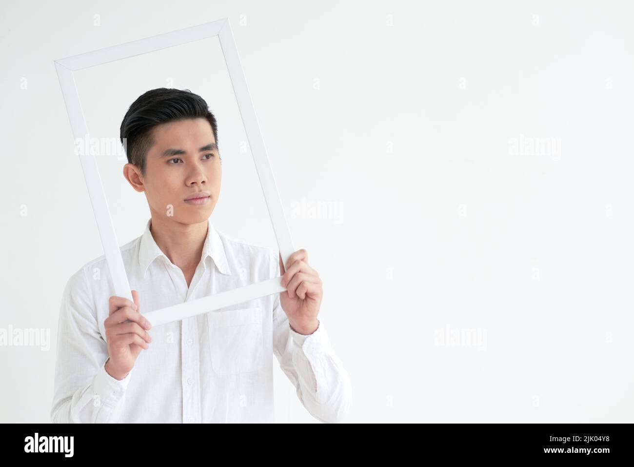 Handsome Vietnamese young man looking through white picture frame Stock Photo