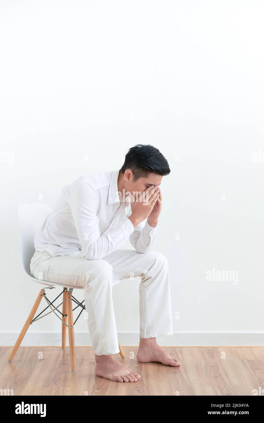 Tired frustrated young man sitting on chair and covering his face with arms Stock Photo