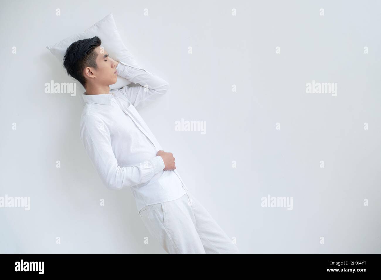 Young man in pajamas sleeping on white floor Stock Photo