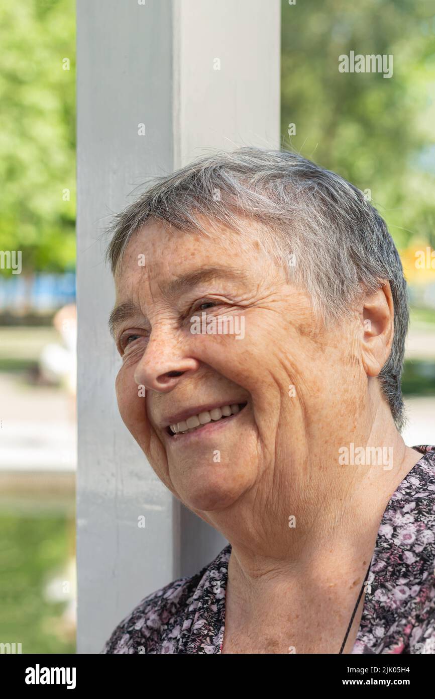 cheerful senior woman chatting with friends, laughing outdoors, looking side. beautiful aged woman enjoying on walk outdoors in summer, National Grand Stock Photo