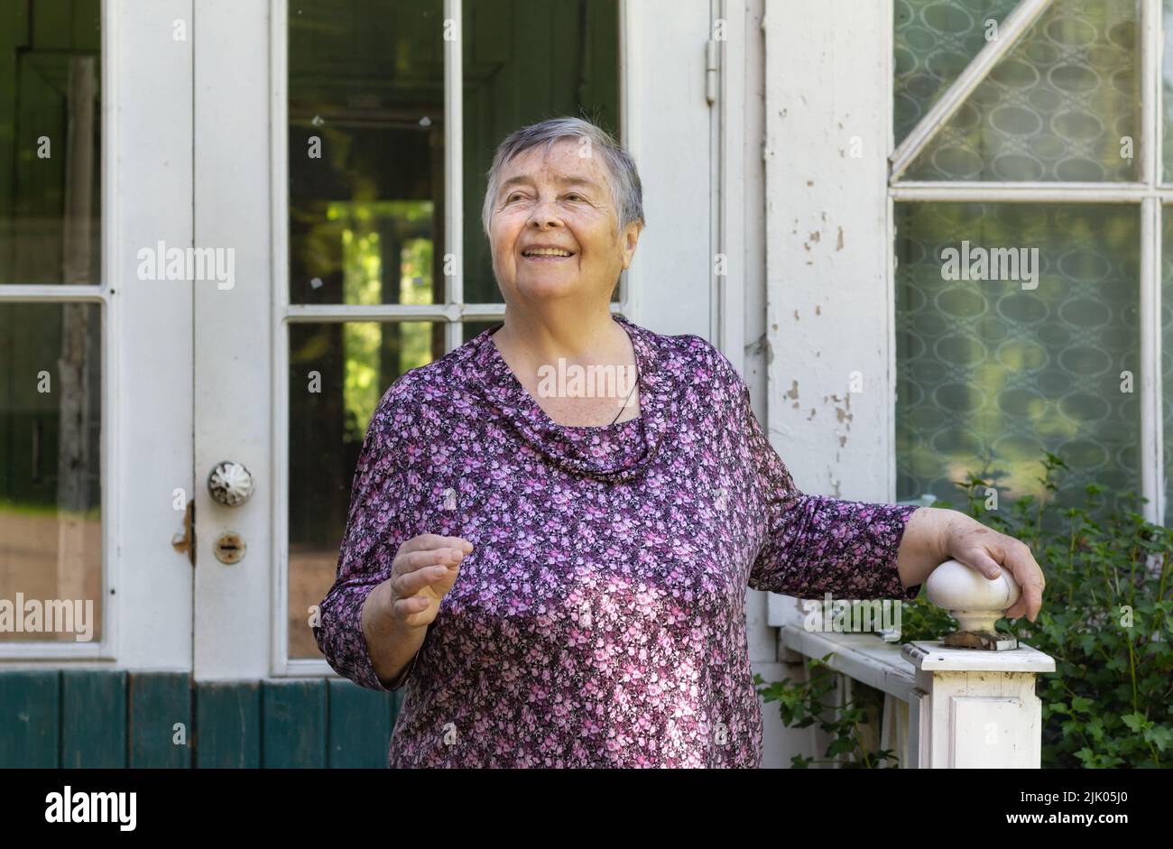 woman welcomes guests on old wooden house background at spring garden. wooden country house with peeling paint on background outside. life concept. Stock Photo