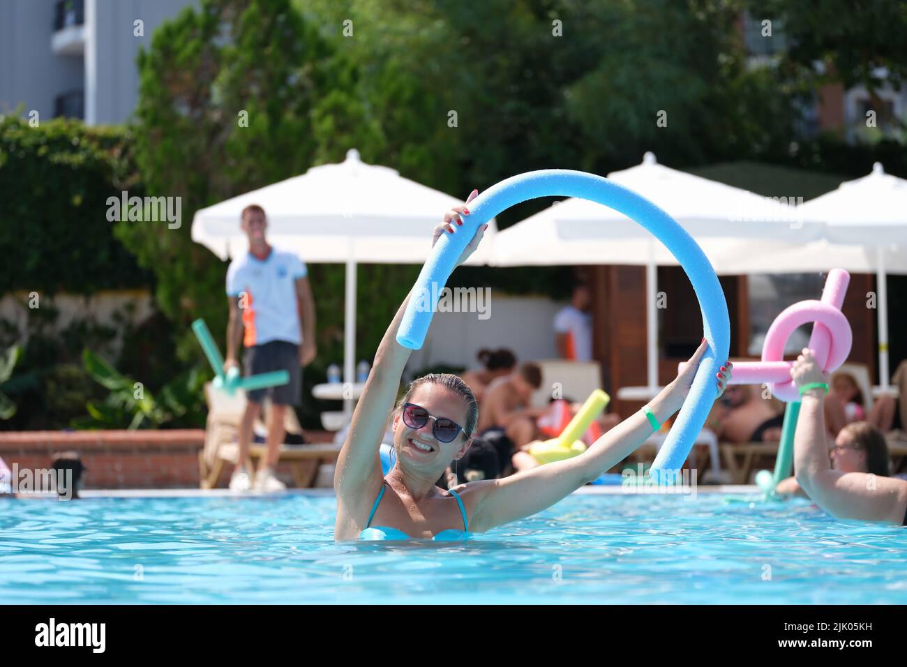 Attractive smiling woman in sunglasses using swimming noodles in pool Stock Photo