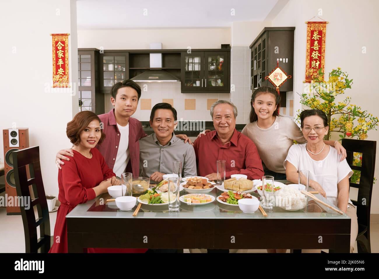 Happy big Vietnamese family having Tet celebration dinner. Scrolls wishing luck and wealth in the background Stock Photo