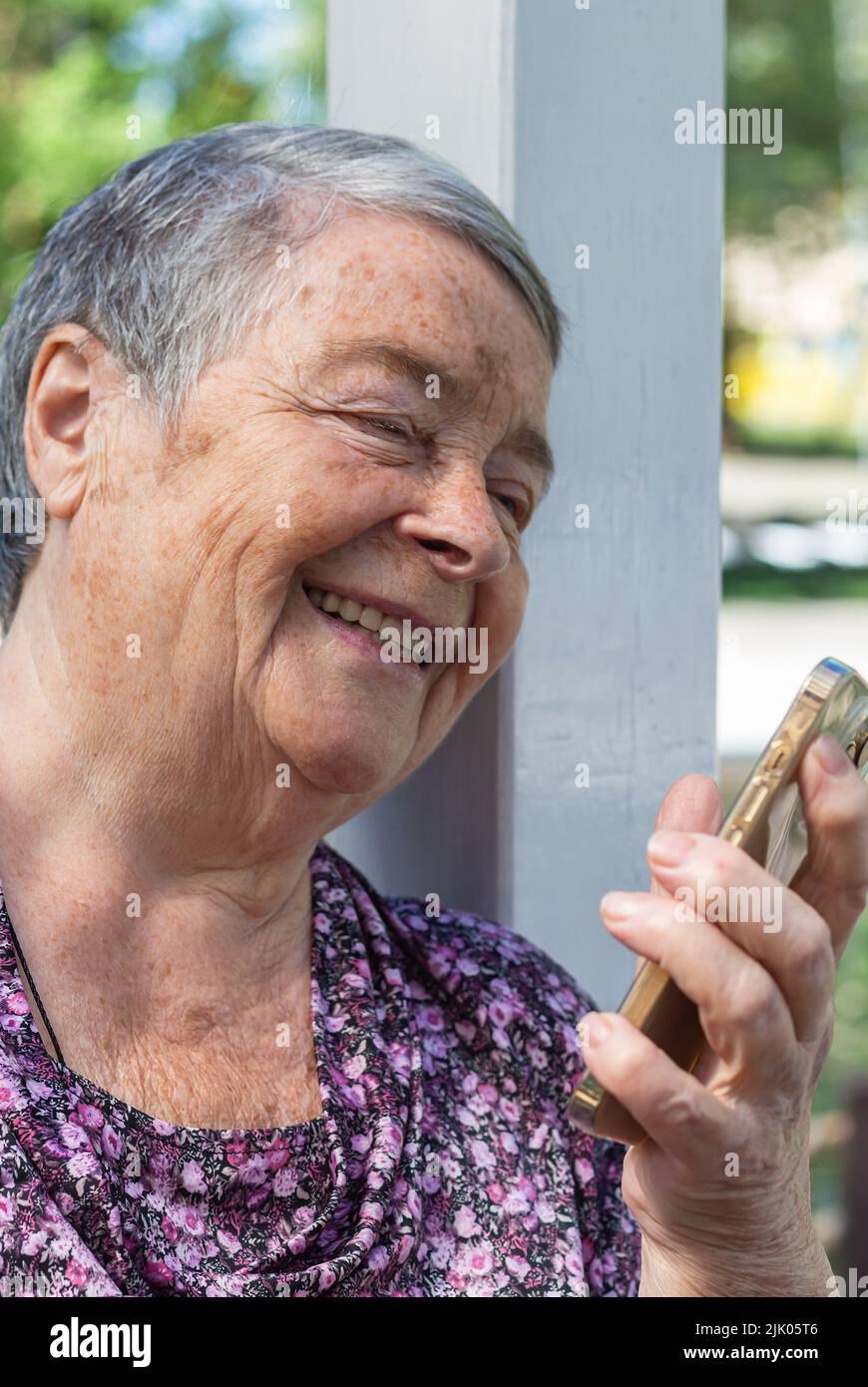 senior woman with smartphone having video call on sunny day in park. Close-up portrait of laughing Senior woman talking on mobile video call, happy Stock Photo