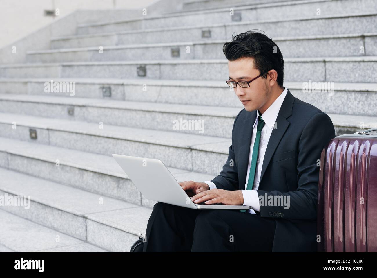 Young businessman sitting outdoors and working on laptop Stock Photo