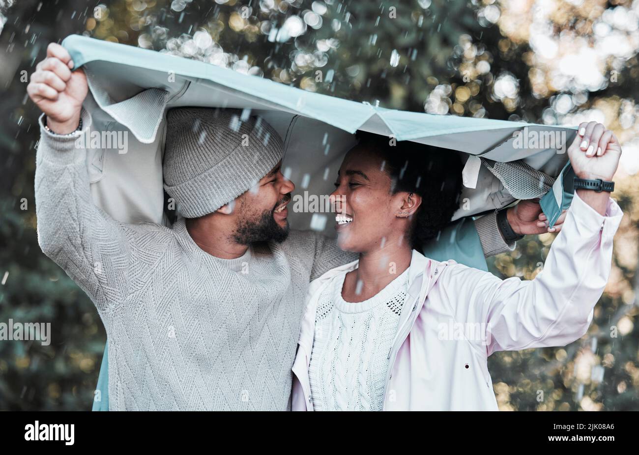 Not even the rain can keep me away from you. a young couple holding a jacket over their heads while out in the rain. Stock Photo