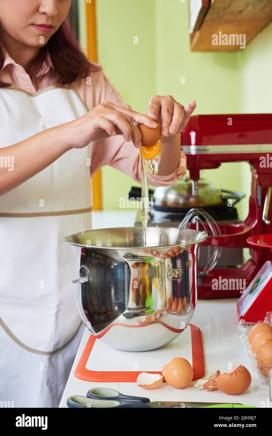 Female baker cracking eggs into mixer bowl to make pie dough Stock