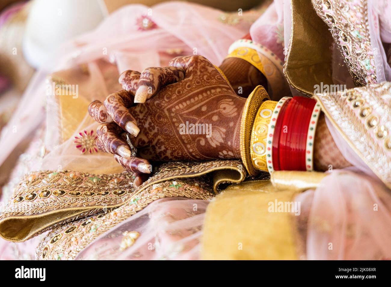 Beautiful Indian bride wearing red bangles and gold jewelry. Mehndi or Henna design on hands. New Indian bride at wedding. Stock Photo