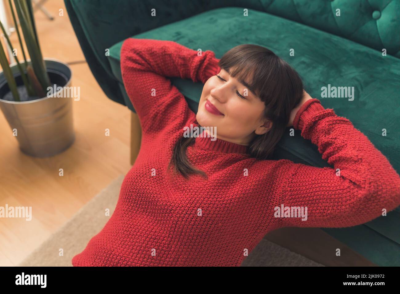 Calm happy young brunette woman wearing a red sweater and relaxing on a couch with her eyes closed. High-quality photo Stock Photo