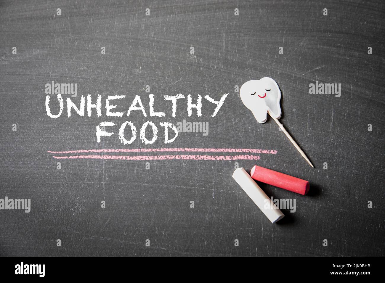 Unhealthy Food. Text and pieces of chalk on a dark blackboard. Stock Photo