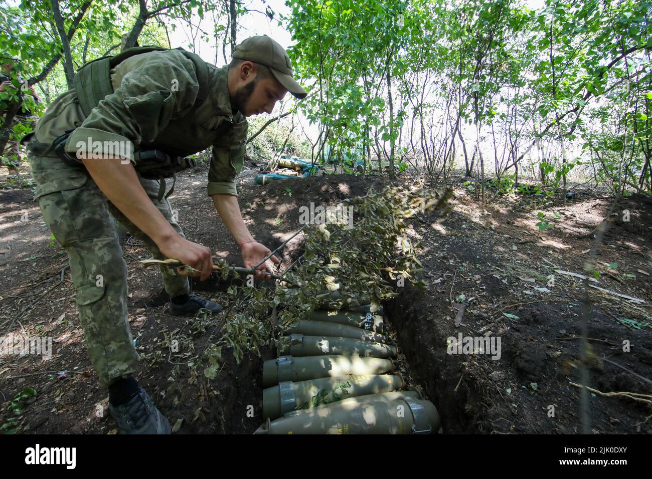 KHARKIV REGION, UKRAINE - JULY 28, 2022 - A Ukrainian serviceman covers ammunition with a camouflage net, Kharkiv Region, northeastern Ukraine. This p Stock Photo