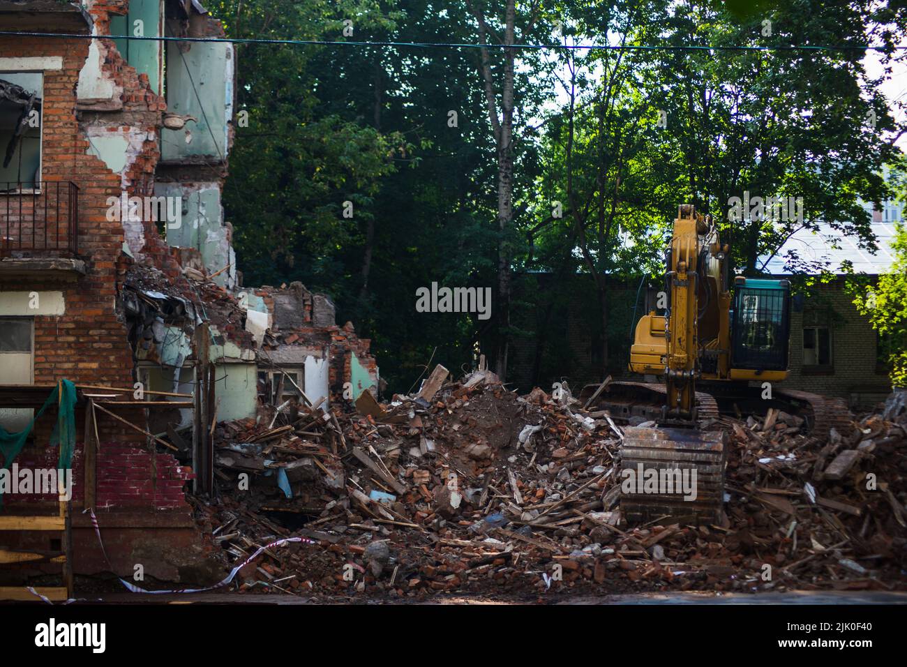 Demolition of a brick building with excavator mechanical arm. Destruction of dilapidated housing. Heavy machinery hydraulic construction equipment Stock Photo