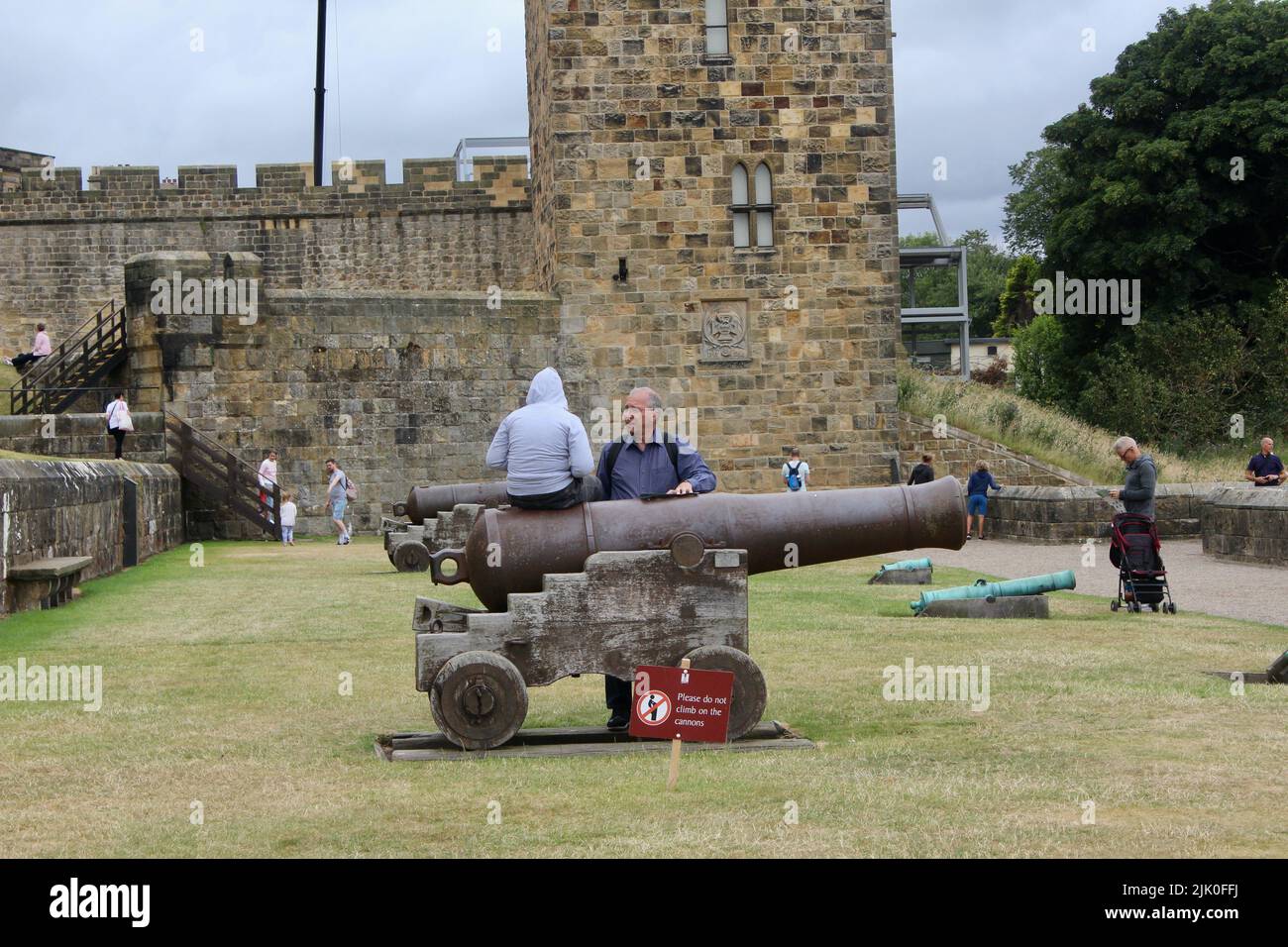 child sitting on a cannon with a do not sit on cannons sign alnwick england UK Stock Photo