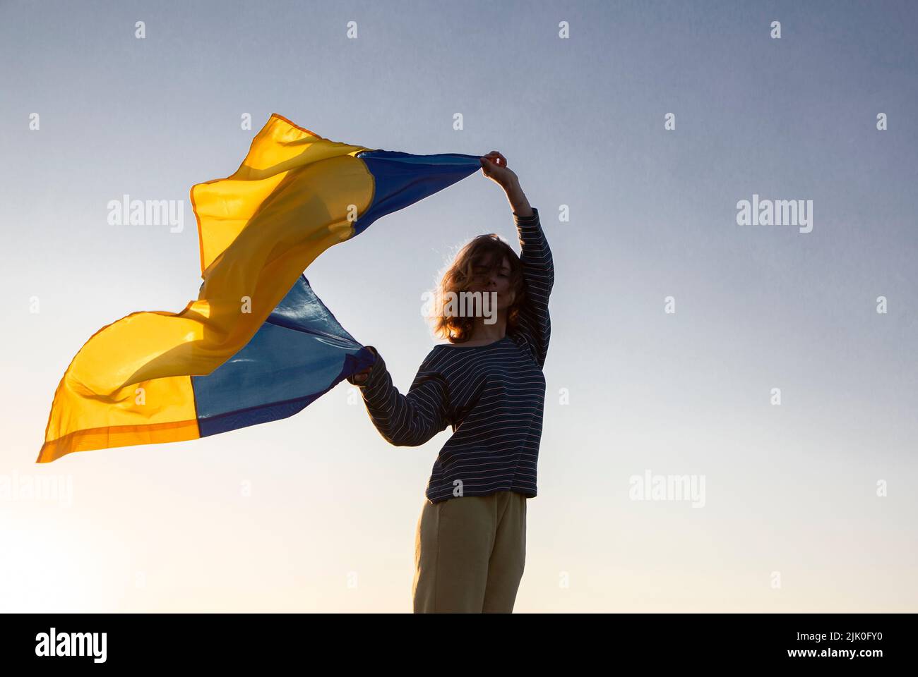 female silhouette with the Ukrainian flag fluttering in the wind against the sky. Ukrainians are against the war. Drawing attention to military operat Stock Photo