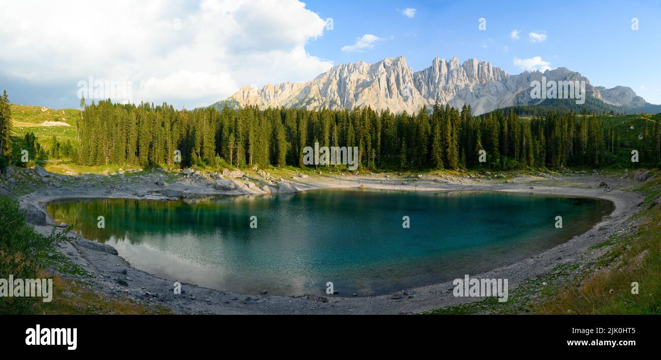 Stunning panoramic view of Carezza Lake (Lago di Carezza) with its emerald green waters, beautiful trees and mountains in the distance. Stock Photo