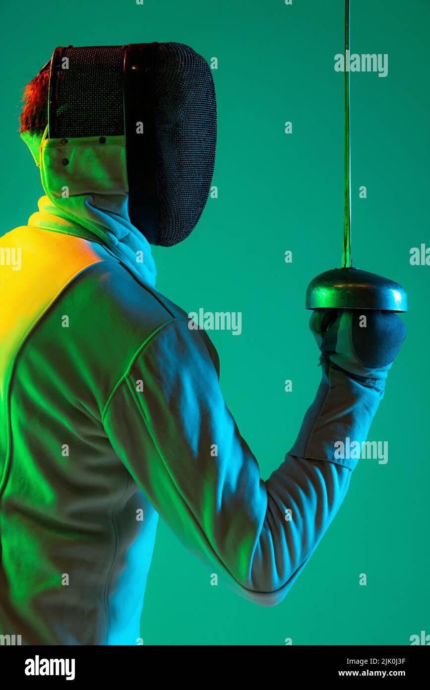 Portrait of young tall male fencer in fencing costume and mask holding