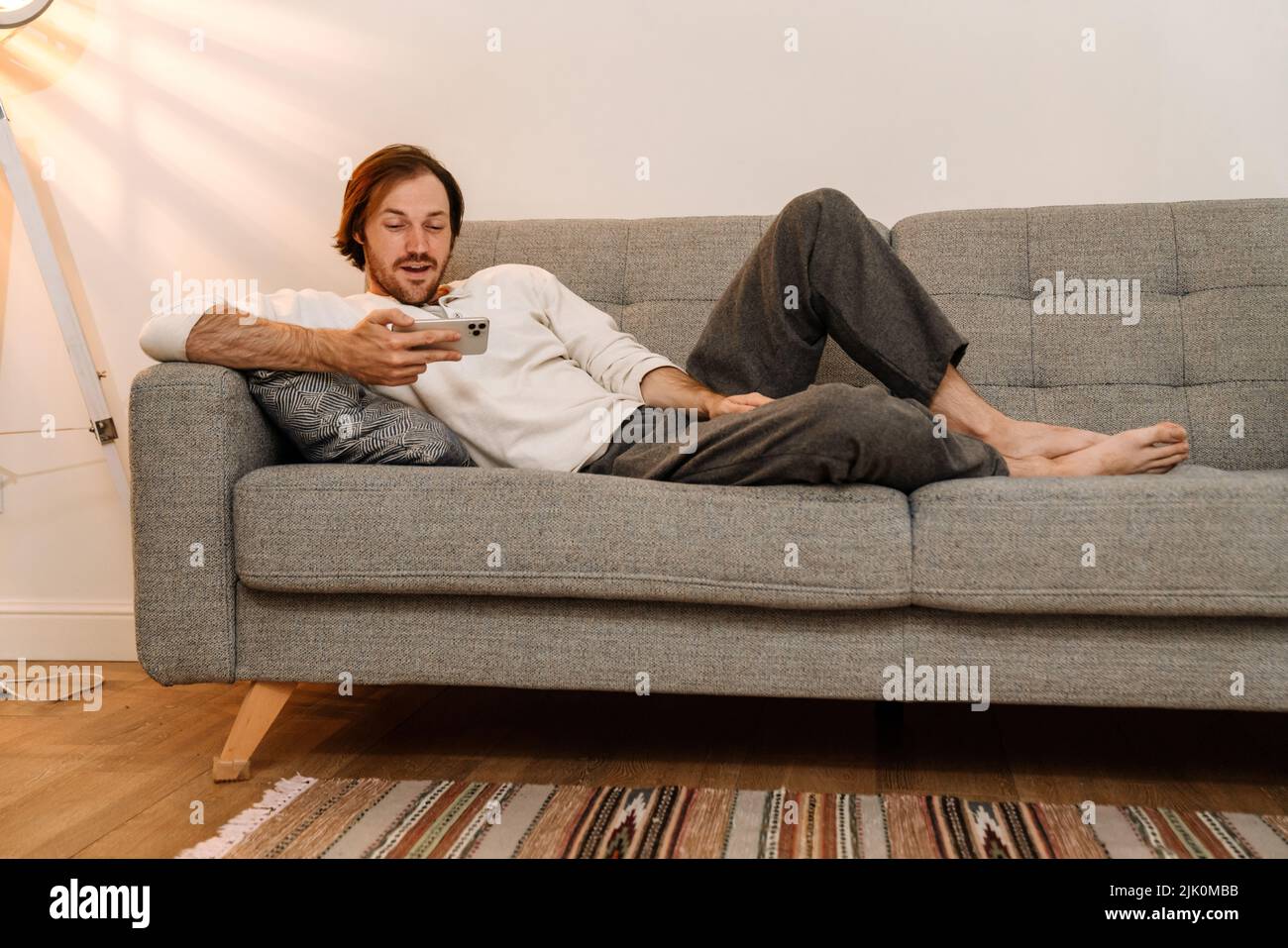 Ginger bristle man using mobile phone while resting on couch at home Stock Photo