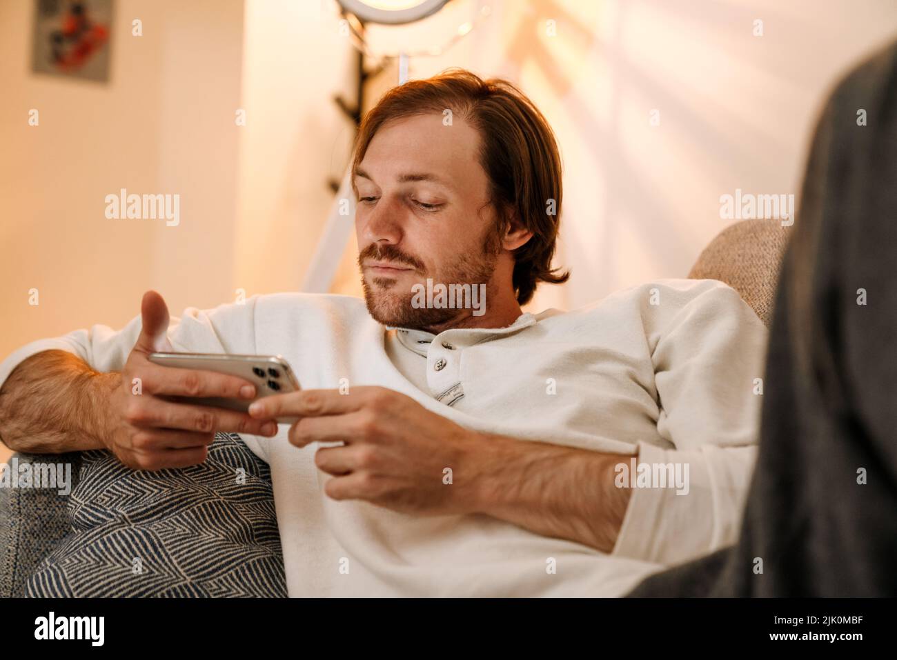Ginger bristle man using mobile phone while resting on couch at home Stock Photo