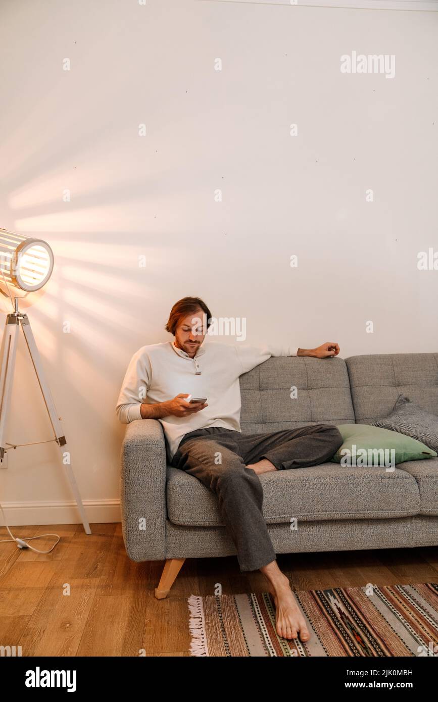 Ginger bristle man using mobile phone while resting on couch at home Stock Photo