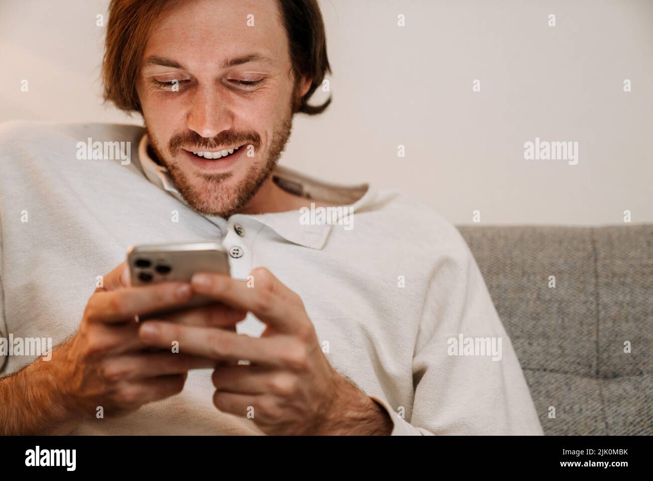Ginger bristle man using mobile phone while resting on couch at home Stock Photo