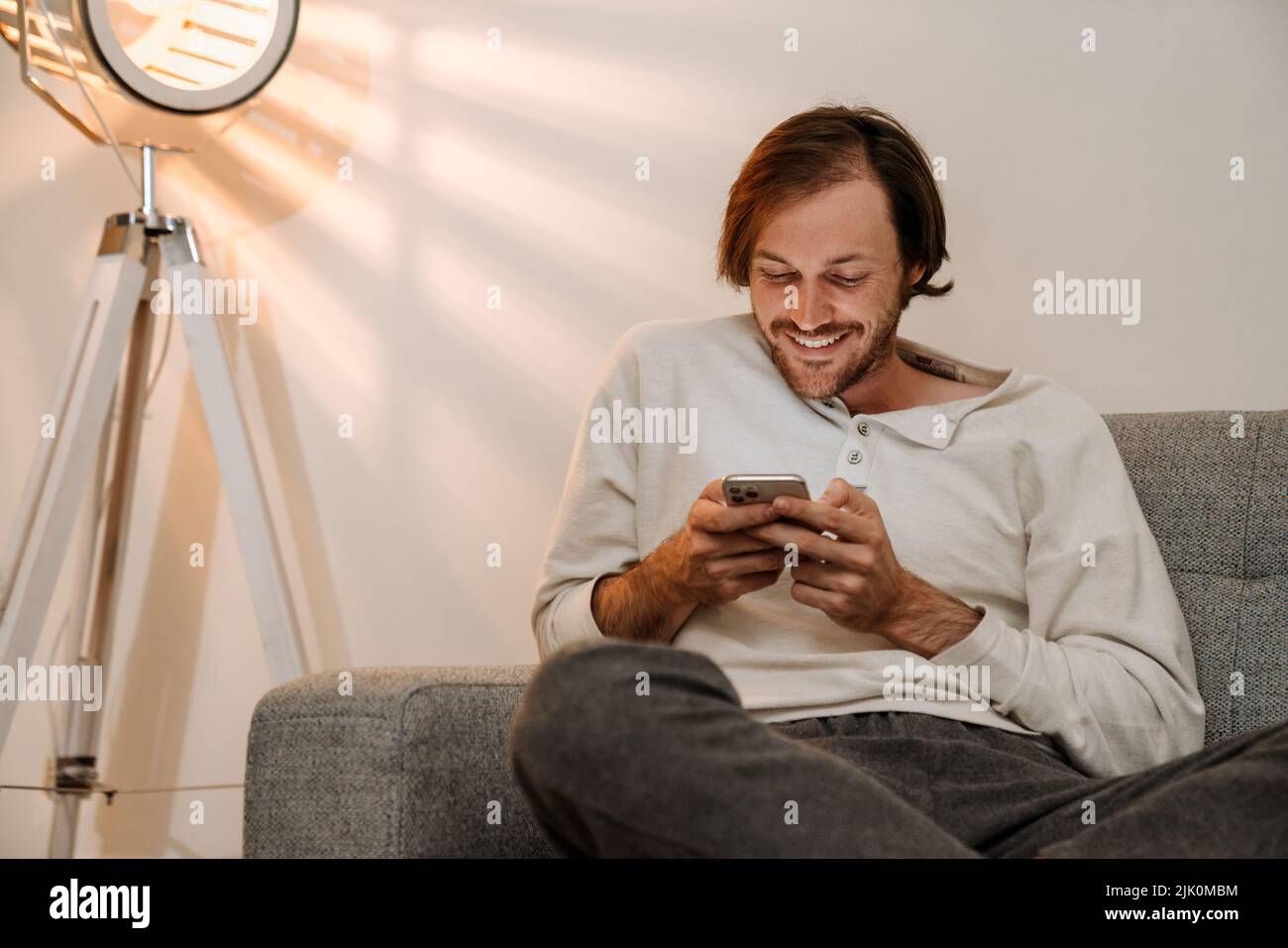 Ginger bristle man using mobile phone while resting on couch at home Stock Photo