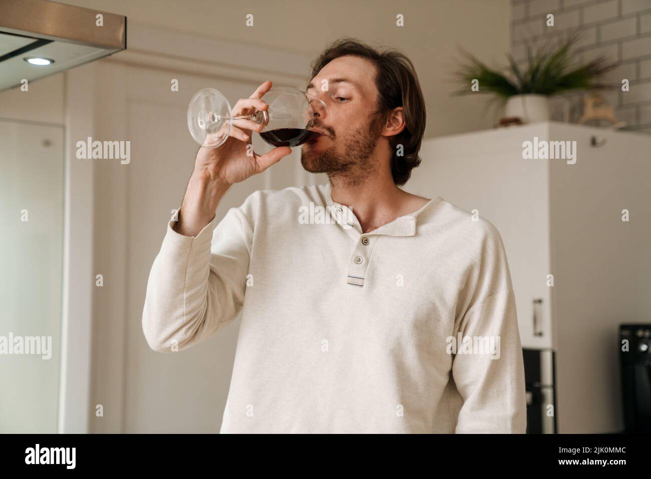 European unshaven man drinking red wine in kitchen at home Stock Photo ...
