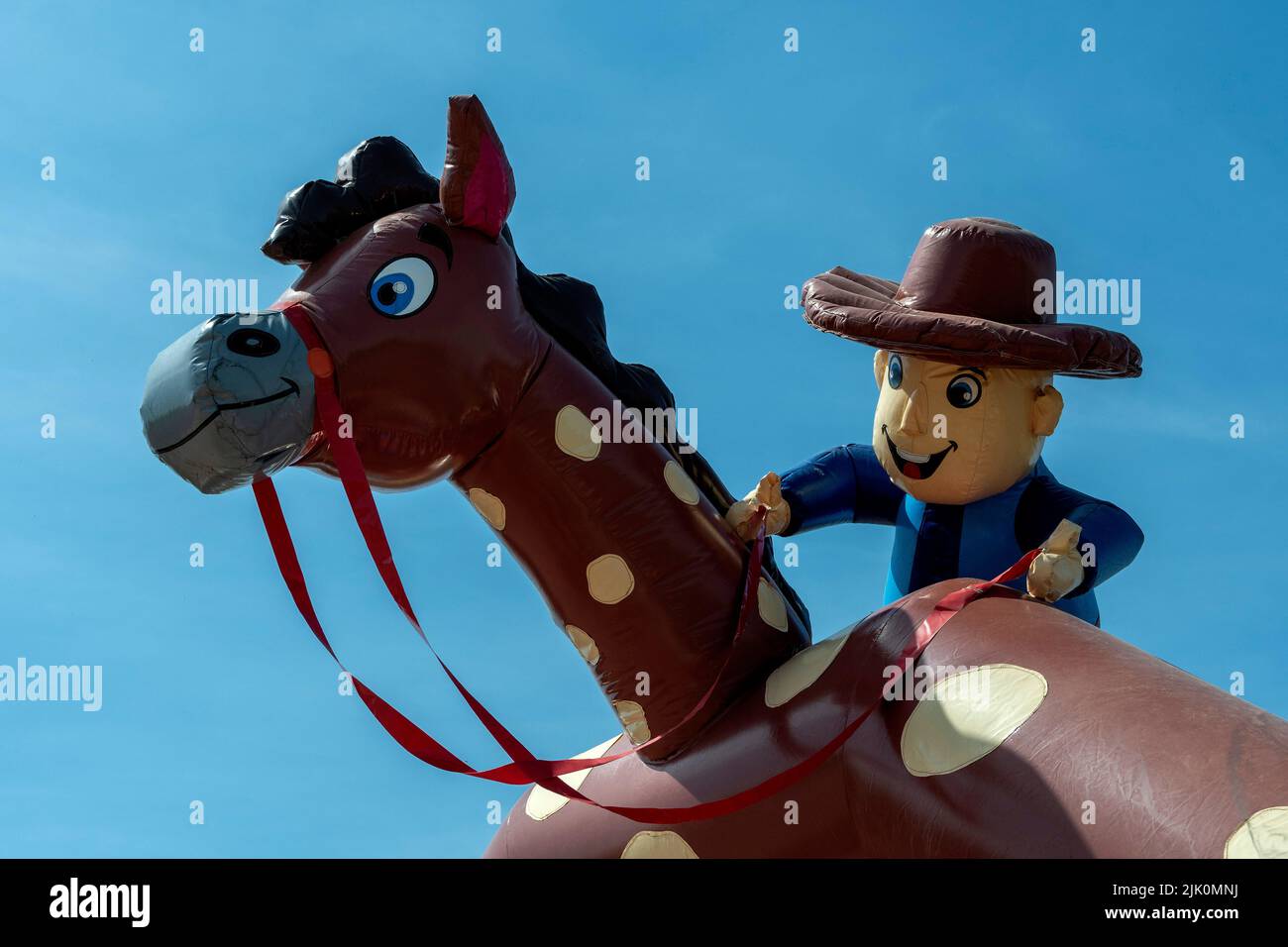 Child character riding a large inflatable horse under a clear blue sky Stock Photo