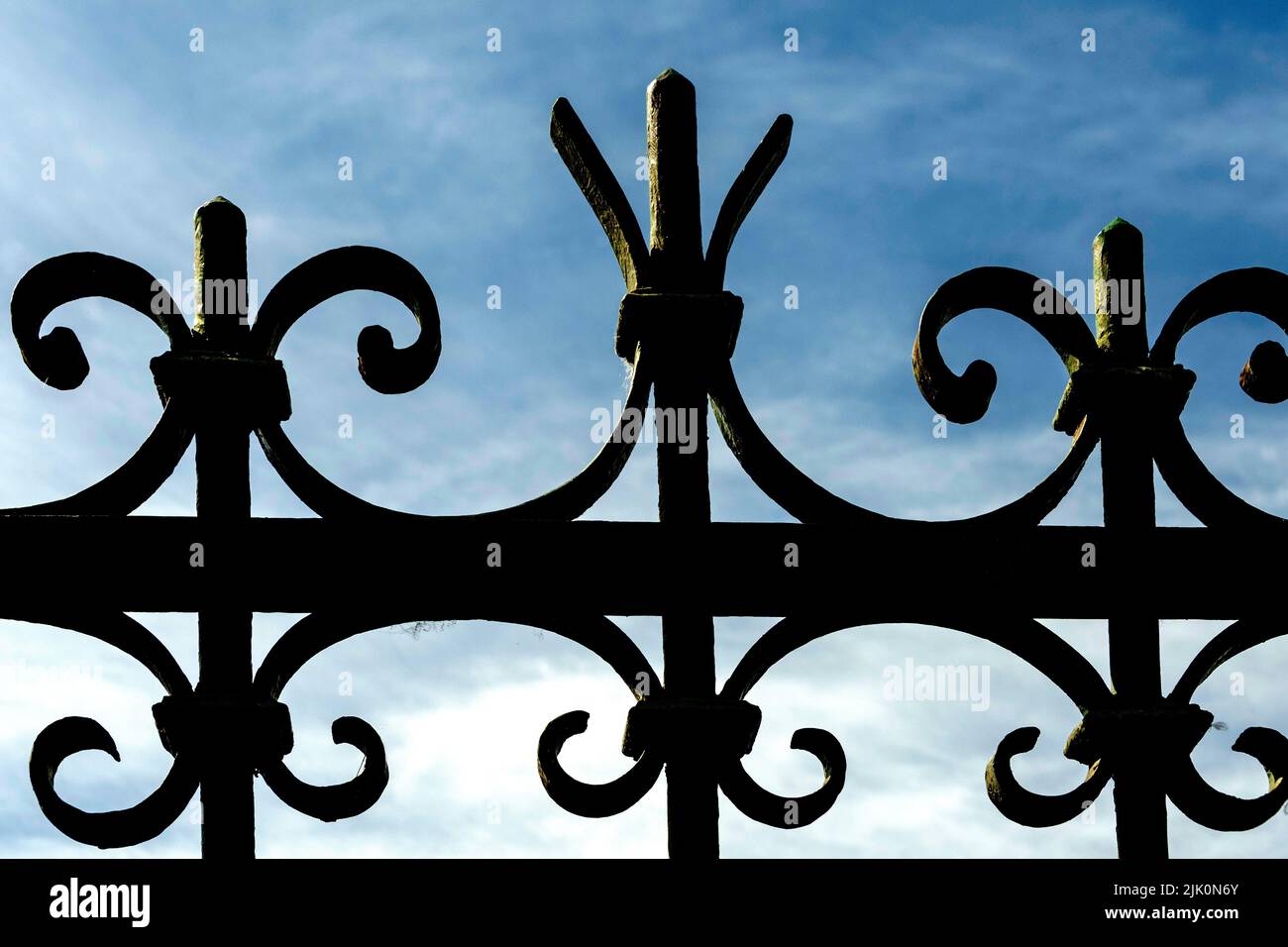 Closeup of a top part of an iron forged fence on the background of blue sky Stock Photo