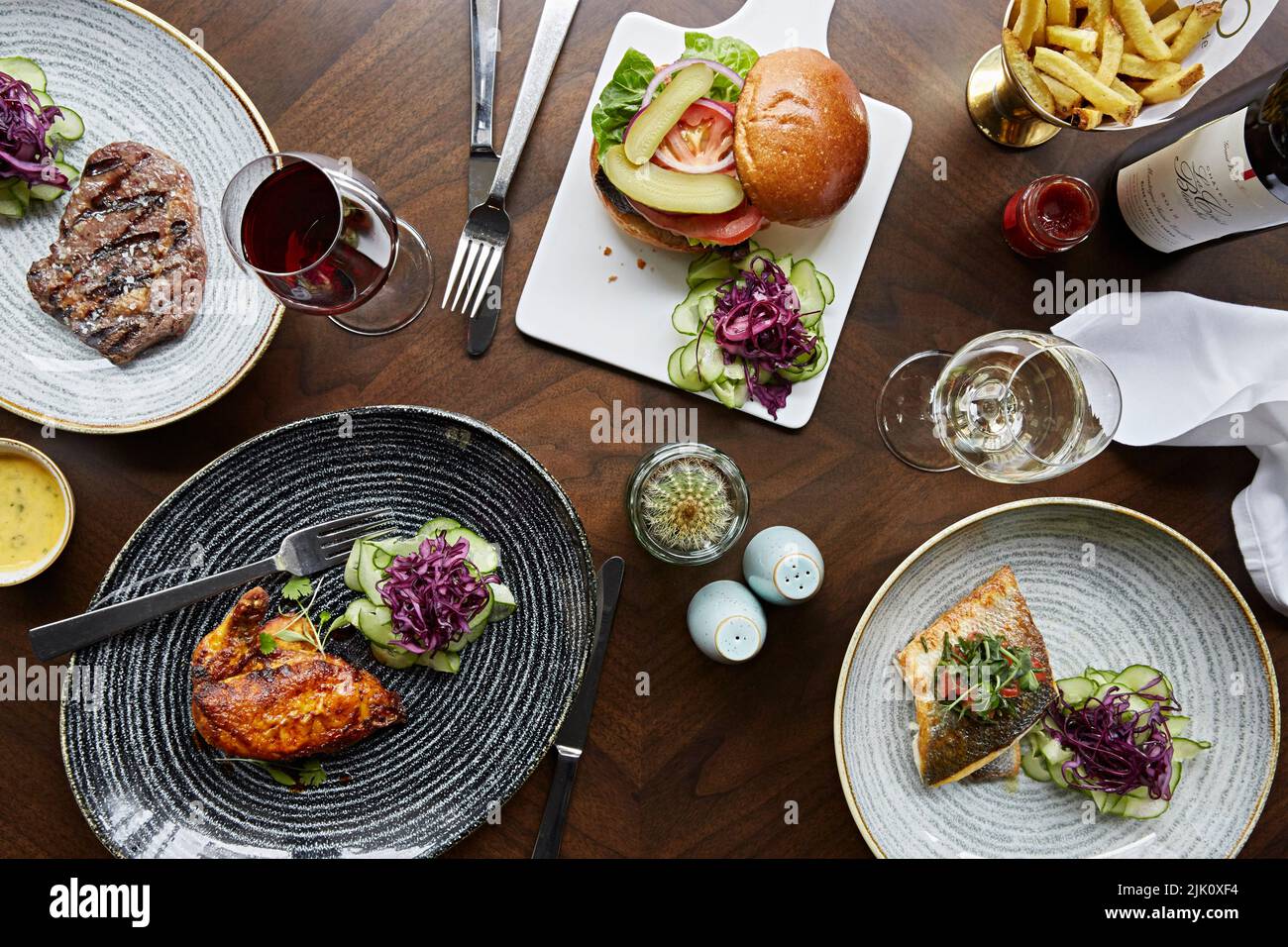 A selection of dishes, steak, chicken, sea bass and a beef burger with fries and wine Stock Photo