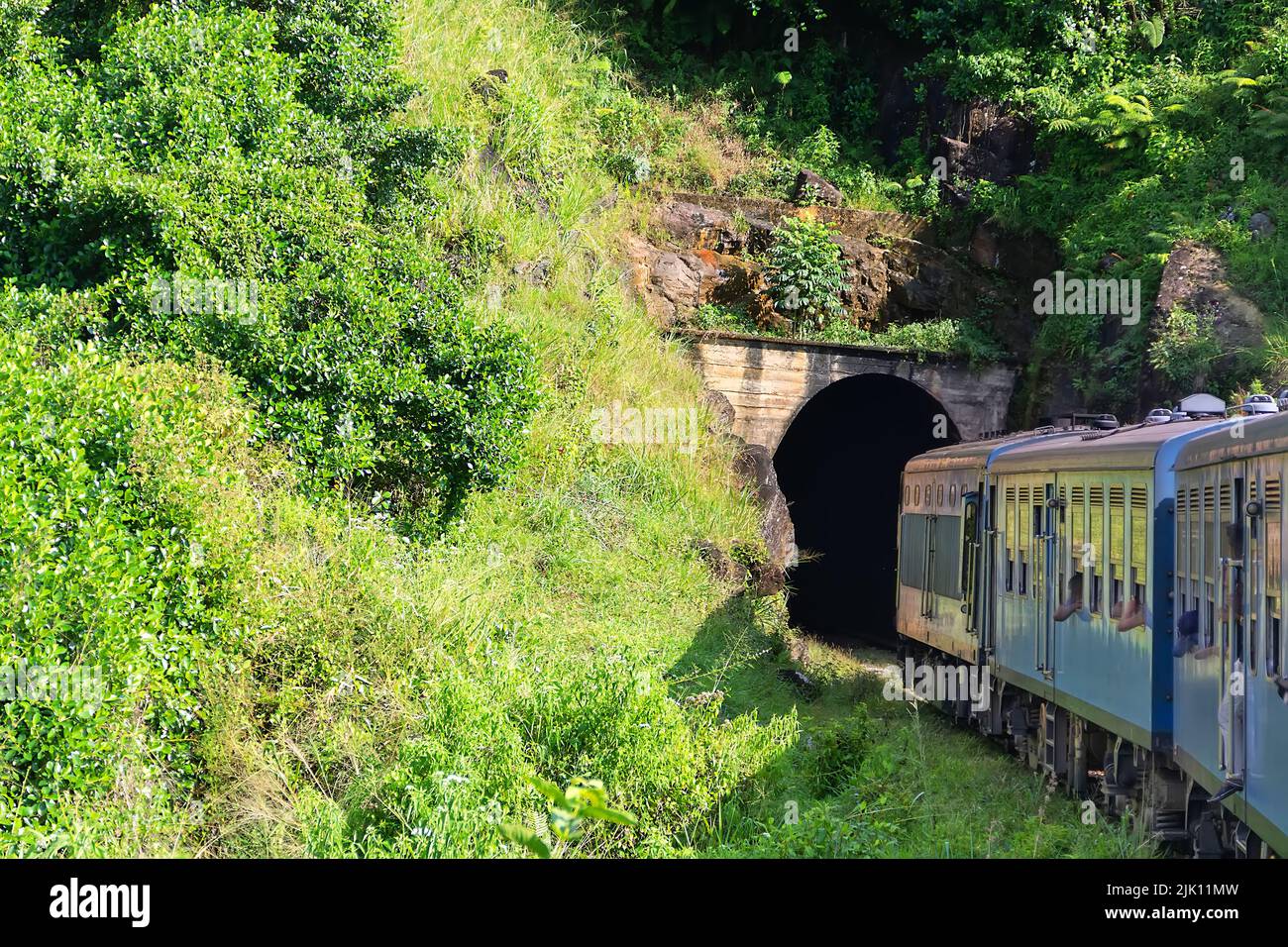 An old passenger train is moving along a mountain railway among the rainforest and rocks. Southeast Asia Stock Photo