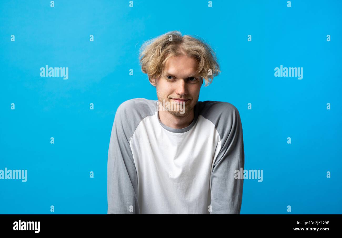 Portrait of young man in long sleeve t-shirt smiling looking at camera over blue background studio. Emotions. Stock Photo
