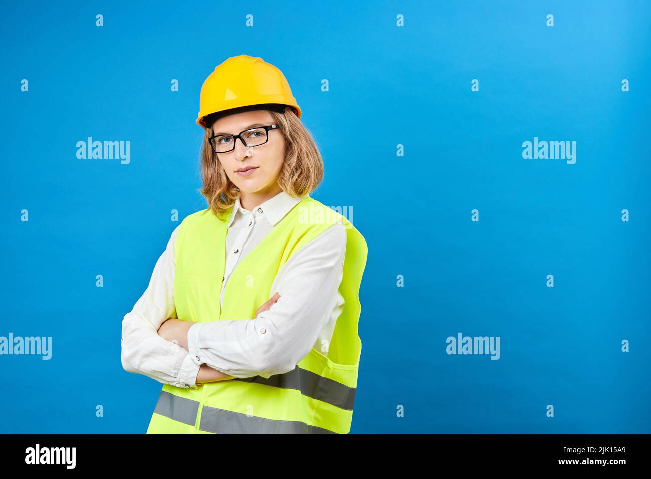 Young woman engineer wearing a yellow helmet, standing in studio on blue background. The concept of construction, repair, decoration Stock Photo