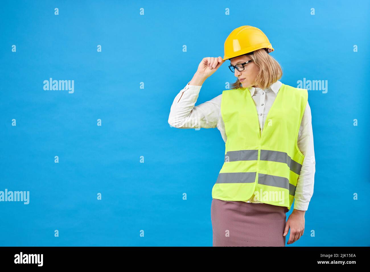 Young woman engineer wearing a yellow helmet, standing in studio on blue background. The concept of construction, repair, decoration Stock Photo