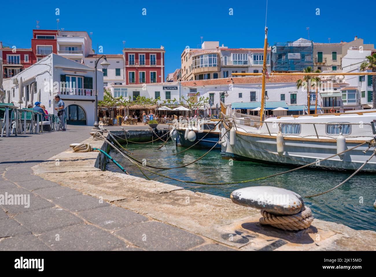 View of colourful cafes, restaurants and boats in harbour against blue sky, Cales Fonts, Menorca, Balearic Islands, Spain, Mediterranean, Europe Stock Photo