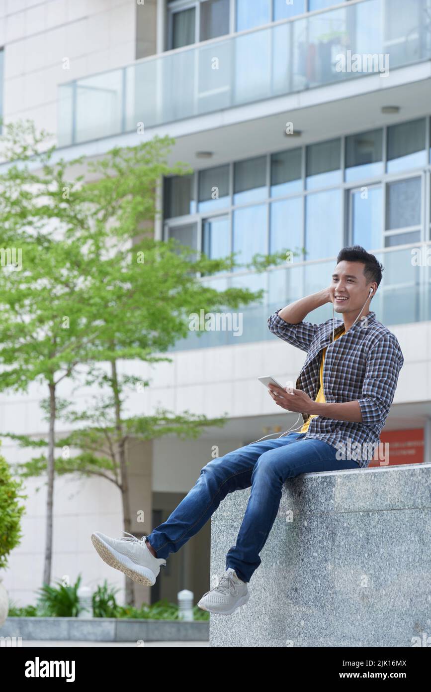 Happy young man with smartphone spending time outdoors Stock Photo